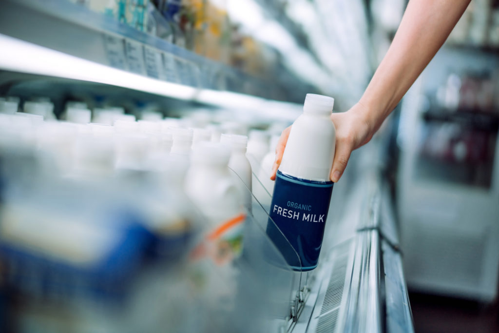 Close up of a woman's hand picking up a bottle of organic fresh milk from the dairy aisle in supermarket. Daily grocery shopping routine. Healthy eating lifestyle